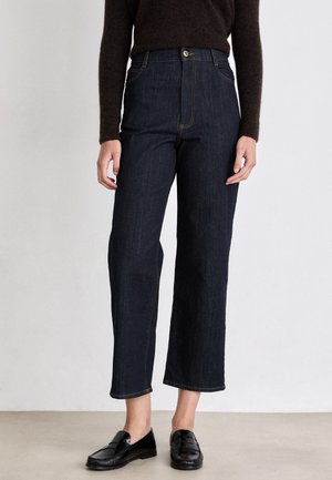 Jeans scuri a vita alta con taglio dritto, cuciture a contrasto e chiusura con bottone, abbinati a mocassini neri.