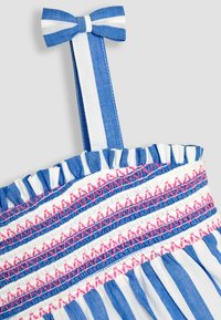 Blouse rayée bleue et blanche, avec un col volanté et un design rose brodé avec un accent de nœud sur la bretelle.