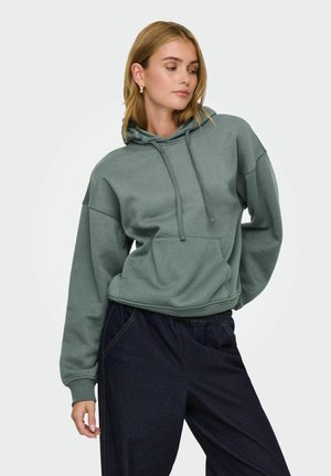 Groene hoodie van zachte stof, met een trekkoord in de capuchon, een voorkzak en een losse pasvorm, gecombineerd met donkere broek. Eenvoudig ontwerp.