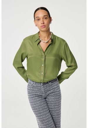 Olive green button-up shirt with a smooth texture, featuring a collar and long sleeves, paired with gray patterned jeans.