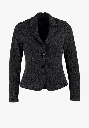 Blazer negro sobre una blusa blanca, combinado con jeans ajustados negros y zapatos de tacón altos color nude, con un tejido texturizado y un ajuste entallado.