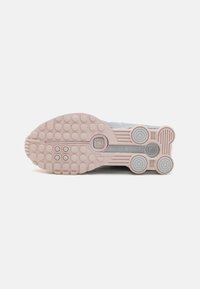 Suela rosa de una zapatilla con patrones de tracción circulares, que presenta acentos grises y un acabado texturizado para agarre y soporte.