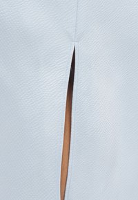 Υφασμάτινο ένδυμα ανοιχτού γαλάζιου χρώματος με υφή και κάθετη σχισμή, εμφανή ραφές κατά μήκος της σχισμής.