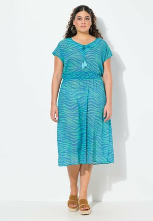 Un vestido color verde azulado con un estampado de cebra y un patrón de texto, que presenta mangas cortas, un detalle de lazo en el cuello y una cintura ajustada. La tela es ligera.