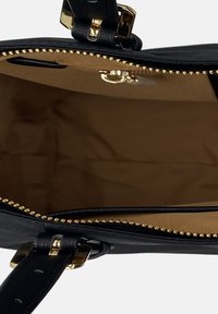 Interno della borsa nera con una fodera liscia di colore marrone chiaro. Zip dorata con dettagli decorativi e manici neri texturizzati.