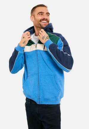 Blauer Kapuzenpullover mit Reißverschluss in einer Farbmischung: Marineblau, Weiß und grüne Akzente. Weicher Stoff, gefütterte Kapuze und Vordertaschen.