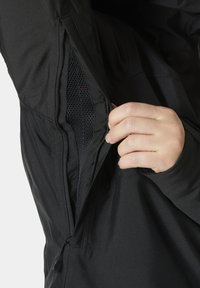 Černá bunda se zipovou kapsou, která má síťovanou podšívku. Tkanina vypadá hladce a lehce, navržena pro funkční nošení.