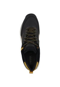 Zapatilla negra con tela texturizada, detalles en amarillo y cordones negros. Presenta una lengüeta acolchada y una suela de goma con una ligera curvatura.