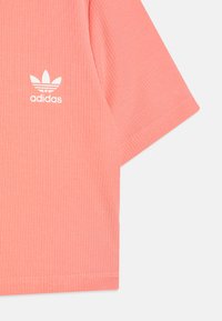 Rozā ribota īsā piedurkne T-krekls ar baltu Adidas logo. Auduma tekstūra ir gluda, ar redzamu ribojumu.