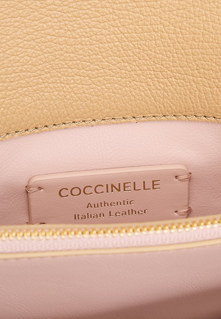 Interno in pelle testurizzata beige con una cerniera dorata, caratterizzato da un'etichetta che recita "Coccinelle Pella Italiana Autentica" in lettere dorate.