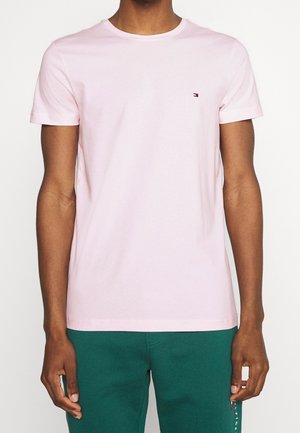 Light pink cotton t-shirt with a crew neckline, short sleeves, and a small red and blue logo on the left chest. Smooth texture.