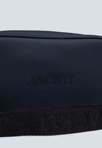 Borsa a pochette navy realizzata in materiale testurizzato con logo "JACK1T" in rilievo e una spessa tracolla nera con un motivo a ripetizione del nome del marchio.