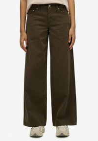 Pantalones de pierna ancha color verde oliva, hechos de algodón, con una cintura alta, bolsillos frontales y una textura suave. Lleva puestos unos zapatillas grises.