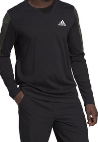 Zwart shirt met lange mouwen en groene accenten op de schouders, met het Adidas-logo op de borst. Gemaakt van een glad, lichtgewicht materiaal.