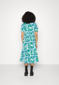 Blommig klänning i nyanser av blått och grönt, med korta puffärmar, smockad midja och ankellång fåll, i sällskap med svarta stövlar.