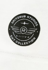 Black circular patch on white fabric with white text "Spitzbub Studios Sky Collection," wings, plane, and a central "R" emblem.