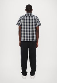 Κοντομάνικο καρό πουκάμισο σε ναυτικό μπλε και λευκό, με ίσια στοά και γιακά, συνδυασμένο με φαρδιά μαύρα παντελόνια και λευκά αθλητικά παπούτσια.