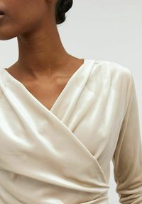 Béžový saténový zavinovací top s nařaseným výstřihem a jemným leskem, s dlouhými rukávy a nařasenými detaily na boku.