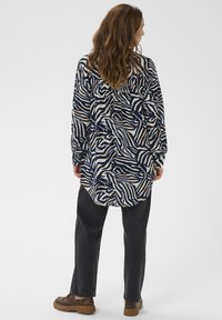 Langærmet skjorte i marineblå med hvid og gylden zebra mønster. Blødt stof med en afslappet pasform, rund kant og knapmanchetter. Parret med mørke jeans og brune sko.