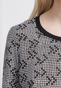 Haut à motifs noir et blanc avec un col rond, en tissu léger, et une texture de petits croix sur l'ensemble du design.