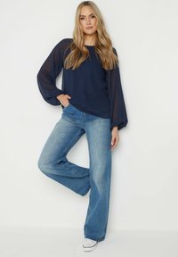 Mörkblå långärmad topp med genomskinliga, texturerade ärmar, ihop med ljusblå vida jeans och vita sneakers.