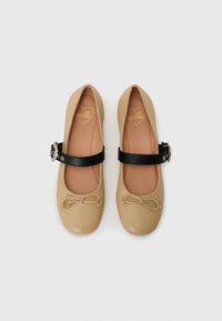 Bežid ballet kingad ümmarguse varbaga, musta pahkluu rihmaga, millel on pandla ja esiküljel dekoratiivne nööp. Sile tekstuur.