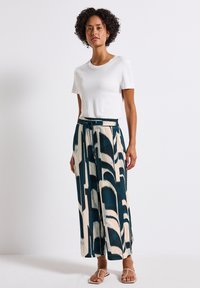 Weißes, enganliegendes T-Shirt, kombiniert mit weit geschnittenen Hosen mit einem abstrakten Muster in Blau und Creme. Die Hose hat einen elastischen Bund und eine Kordel.