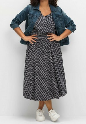 Navyjurk met bloemmotief, een aangesloten lijfje en een uitlopende rok, gecombineerd met een spijkerjasje en witte sneakers.