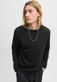 Schwarzes Langarmshirt aus weichem Stoff mit lockerer Passform, ausgestattet mit einem Rundhalsausschnitt und dezenten Nähdetails. Kombiniert mit gestreiften Hosen.