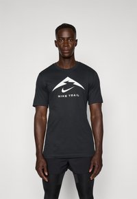 Schwarzes Baumwoll-T-Shirt mit Rundhalsausschnitt, versehen mit einem weißen Nike-Logo und dem Text "NIKE TRAIL" unter einem dreieckigen Design. Kurze Ärmel.