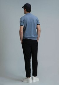 Polo bleu clair à manches courtes avec des rayures blanches et foncées aux poignets, associé à un pantalon noir et des baskets blanches. Design clair et structuré.