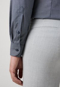 Tengerészeti és fehér mintás pólóing gombos mandzsettával, világosszürke nadrágok mellett bemutatva, sima textúrákkal és testhezálló szabással.