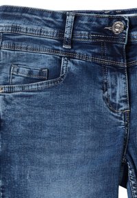 Jean en denim bleu moyen avec une texture lisse, doté d'une poche avant, d'une fermeture par bouton métallique et de surpiqûres dorées contrastantes le long des coutures.