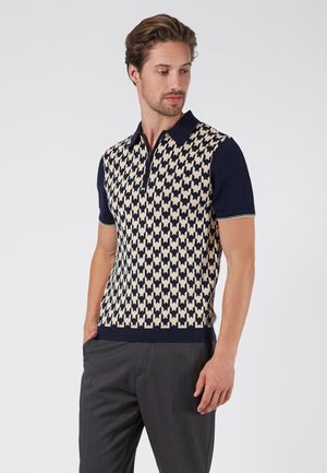 Polo à manches courtes avec un motif pied-de-poule bleu marine et crème, doté d'un col zippé et d'une coupe ajustée, fabriqué en tissu tricoté.