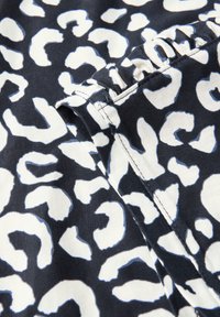 Leopardmönstrad tyg med vita och ljusblå former på en svart bakgrund. Nära detalj visar söm och mjuk textur.