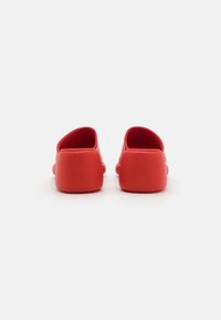 Sapatos vermelhos slip-on com uma textura suave, salto arredondado e um design minimalista com uma altura modesta e estilo sem costas.