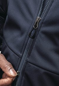 Navy fleece jacket with zip closure, textured fabric, visible stitching, and a hand gripping the zipper pull for adjustment.