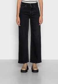 Czarne dżinsy z szerokimi nogawkami z wysokim stanem, cztery kieszenie i szlufki na pasek, zestawione z beżowymi masywnymi butami na platformie.