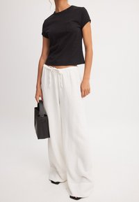 Must mustama t-särk lühikeste varrukatega ja rinnataskuga, millele on sobitatud laiad valged tekstureeritud püksid ja väike must kott.