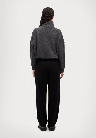 Grå strikket sweater med høj krave, løs pasform og dropped skuldre, parret med sorte vide bukser og kraftige sorte sko.