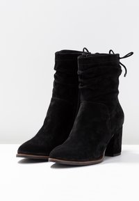 Bottes cheville en daim noir avec un design froncé, bout pointu et talon bloc. Dotées de lacets en haut et d'une fermeture éclair latérale.