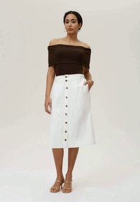 Saia midi de ganga branca com fecho frontal de botões e bolsos. Combinada com uma blusa castanha de ombro à mostra. Textura suave, ajuste perfeitamente moldado.
