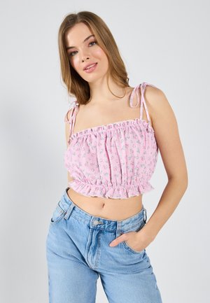 Top scurt floral roz cu tiv ondulat și bretele ajustabile, asortat cu blugi ușori, cu talie înaltă, de culoare albastru deschis. Țesătură moale, texturată.