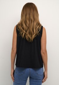 Top senza maniche nero con una vestibilità ampia, realizzato in tessuto leggero, caratterizzato da un collo rotondo e dettagli di pieghe sul retro. Abbinato a jeans blu.