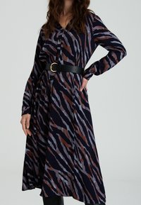 Robe à boutons navy avec un motif en rayures de tigre dans des tons de marron et de gris, dotée de manches longues et d'une ceinture noire. Texture de tissu lisse.