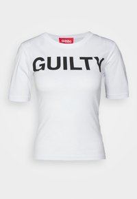 Camiseta de algodón blanca de manga corta, con un audaz texto negro "GUILTY" en el frente y una etiqueta de marca roja en el escote.