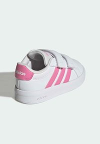 Bílá teniska s růžovými pruhy a akcenty, suchými zipy, hladkým koženým svrškem, polstrovaným límcem a gumovou podrážkou.