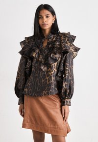 Blus dengan motif leopard dengan desain berkerut, skema warna hitam dan coklat, lengan panjang, dan leher kunci. Dipadukan dengan rok kulit coklat.