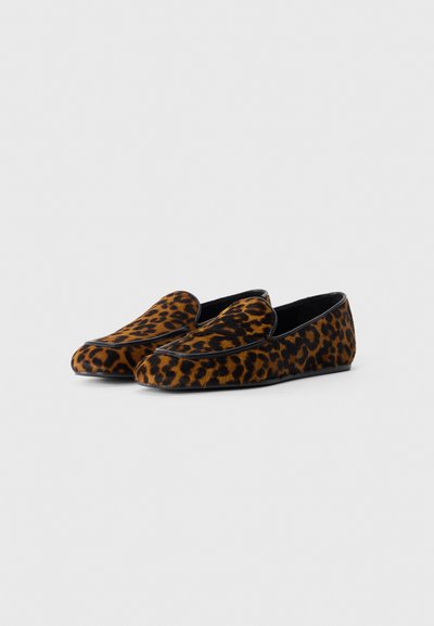 Une paire de mocassins à enfiler au motif léopard et aux bordures noires, présentée sur un fond blanc.