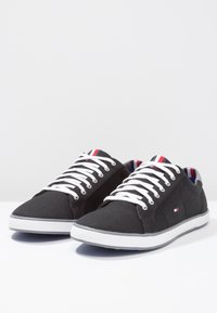 Sneakers neri in tela con lacci bianchi, suole in gomma e un motivo a righe sulla fodera interna. Dettaglio del logo sul lato.